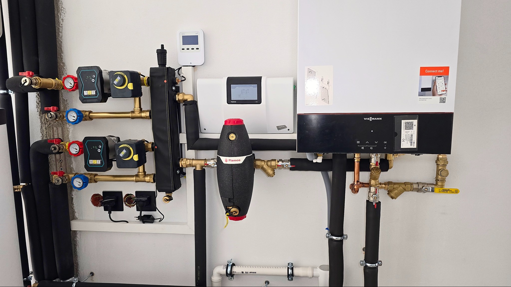 Złożona instalacja grzewcza z kotłem Viessmann, pompami obiegowymi RZT, zbiornikiem Flamco i sterownikiem TECH, widoczne liczne rury, zawory i manometry.