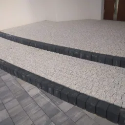 Wykończony podjazd z jasnoszarej kostki brukowej oddzielony ciemnoszarą obwódką z kostki, widok z dołu pod lekkim kątem.