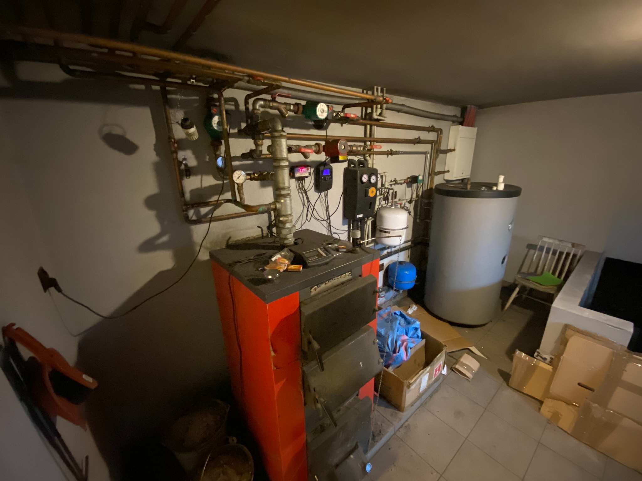 Kotłownia z kotłem na paliwo stałe, instalacją grzewczą z rur miedzianych, zbiornikiem akumulacyjnym i osprzętem, w pomieszczeniu z płytkami podłogowymi.