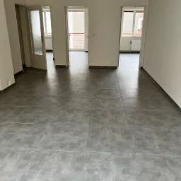 Ułożona, szara, matowa podłoga z płytek w pustym mieszkaniu w Dębicy, widoczne drzwi do innych pomieszczeń.