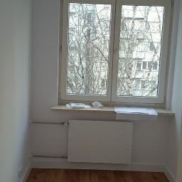 PAWLAN-PROJEKT Pavlo Kulbakov - Pusty pokój po remoncie z panelami podłogowymi w odcieniach brązu, białymi ścianami, grzejnikiem i klimatyzatorem, widok z okna na drzewa bez liści.