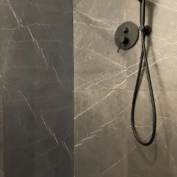 Nowoczesna kabina prysznicowa z ciemnoszarymi płytkami imitującymi marmur i czarną armaturą, w tym deszczownicą i baterią.