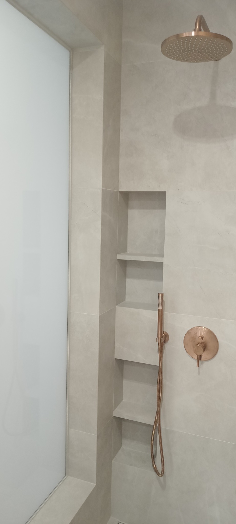 Wykończona kabina prysznicowa z półkami wnękowymi, armaturą w kolorze różowego złota i szklanymi drzwiami.