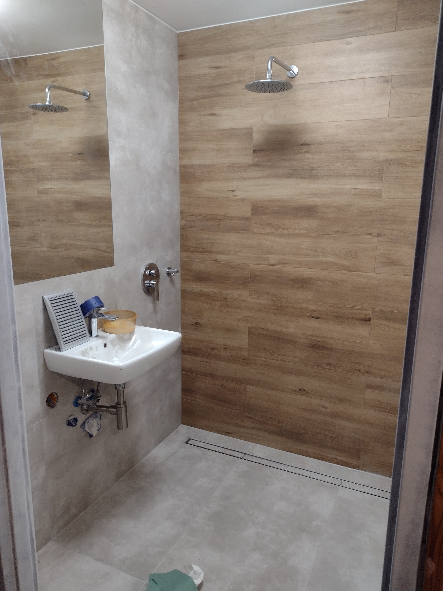 Nowoczesna łazienka z kabiną prysznicową typu walk-in, wykończona płytkami imitującymi drewno na ścianie prysznica i szarymi płytkami na pozostałych ścianach i podłodze, z umywalką nablatową...