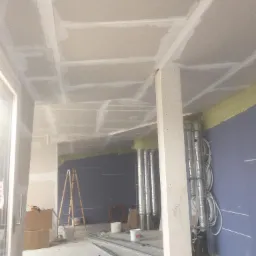 Montaż płyt gipsowo-kartonowych na suficie w trakcie prac wykończeniowych; widoczne profile, drabina i instalacje wentylacyjne.