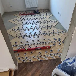 Układanie płytek imitujących parkiet w jodełkę; widoczne poziomica, system poziomowania płytek, oraz częściowo ułożona podłoga w drugim pomieszczeniu