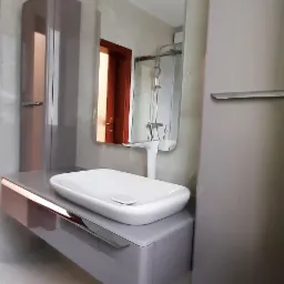 Nowoczesna łazienka z umywalką nablatową, szafką pod umywalką w kolorze taupe z miedzianymi akcentami, lustrem i wysoką szafką, widok na kabinę prysznicową w odbiciu lustra.