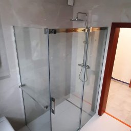 LukFed - Nowoczesna kabina prysznicowa ze szklanymi drzwiami i chromowanym wykończeniem, zamontowana w łazience z beżowymi płytkami imitującymi marmur i białymi płytkami podłogowymi, z widocznym fragmentem...