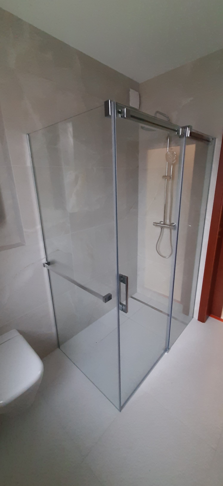 Nowoczesna kabina prysznicowa z przesuwnymi drzwiami ze szkła hartowanego, zamontowana w wykończonej łazience z beżowymi płytkami i białą armaturą.