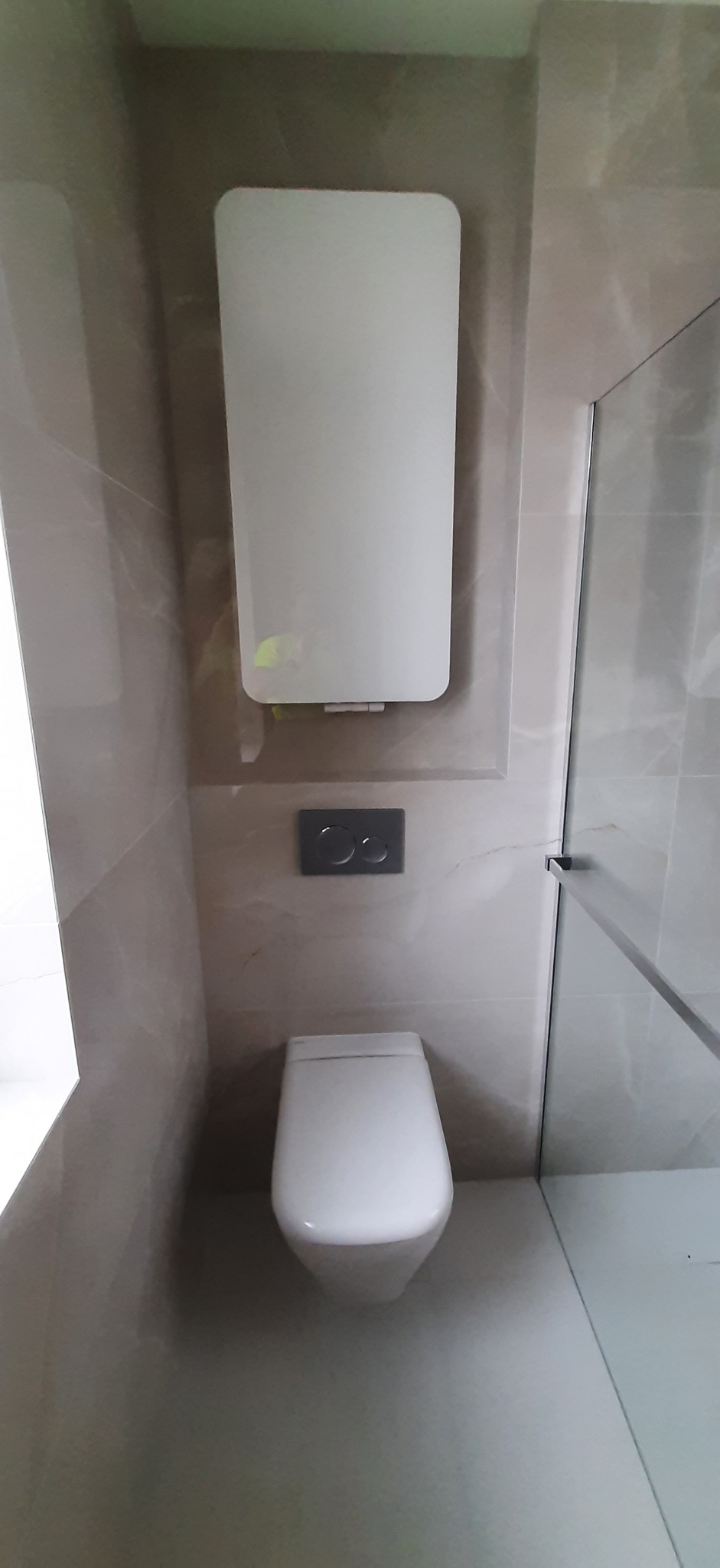 Nowoczesna łazienka z podwieszaną toaletą, beżowe płytki imitujące marmur, szklana kabina prysznicowa i grzejnik elektryczny.