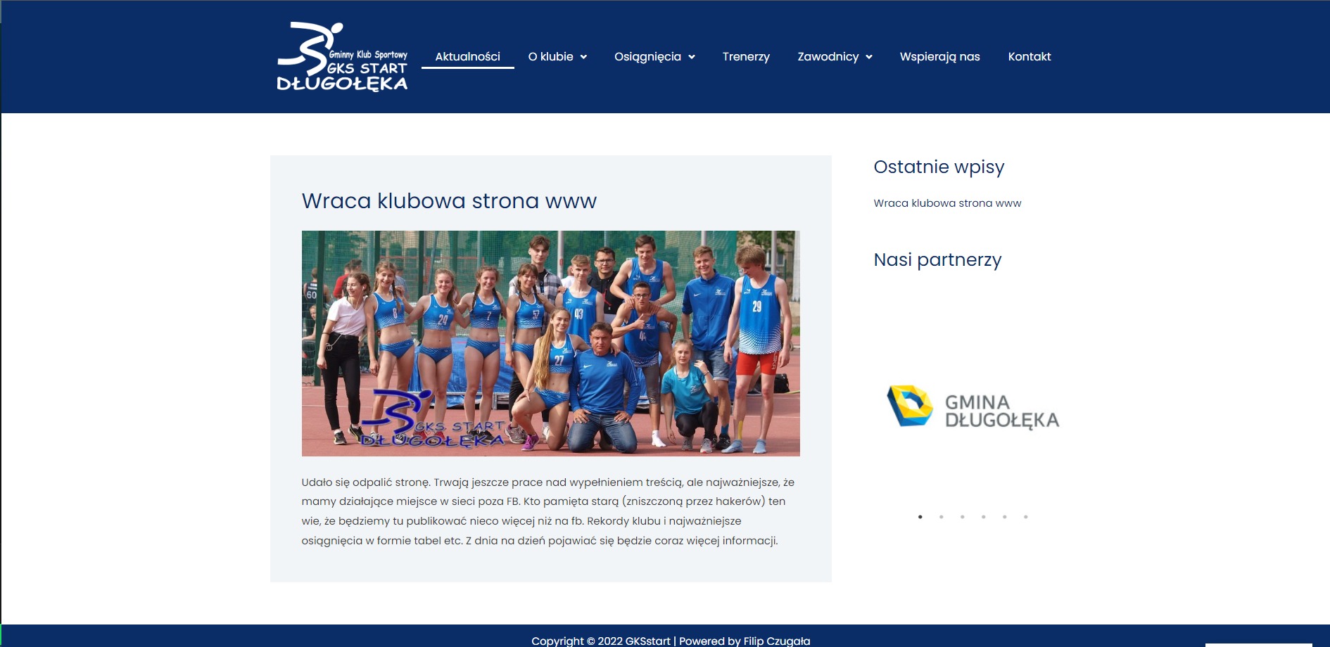 Zdjęcie grupowe sportowców Gminnego Klubu Sportowego Start Długołęka na tle stadionu, prezentowane na stronie internetowej gksstart.pl, z widocznym logo klubu w lewym dolnym rogu i tekstem 'Wraca...