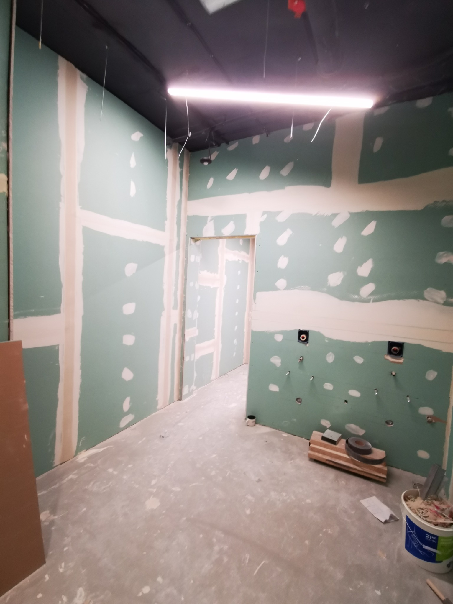 Wnętrze w trakcie montażu płyt gipsowo-kartonowych, widoczne szpachlowane łączenia, otwory instalacyjne i narzędzia na podłodze.