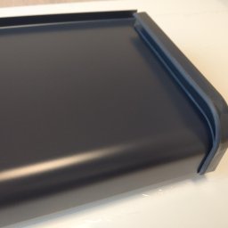 Ideal Rafał Dyro - Fragment ciemnoszarego parapetu aluminiowego z charakterystycznym profilem krawędzi, leżącego na jasnej powierzchni.