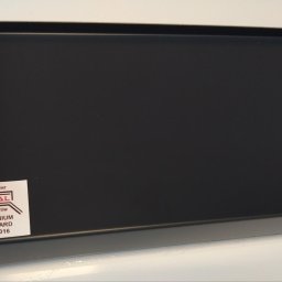 Ideal Rafał Dyro - Szary, aluminiowy parapet z naklejką producenta 'IDEAL', przedstawiającą standard RAL 7016, sfotografowany na białym tle.