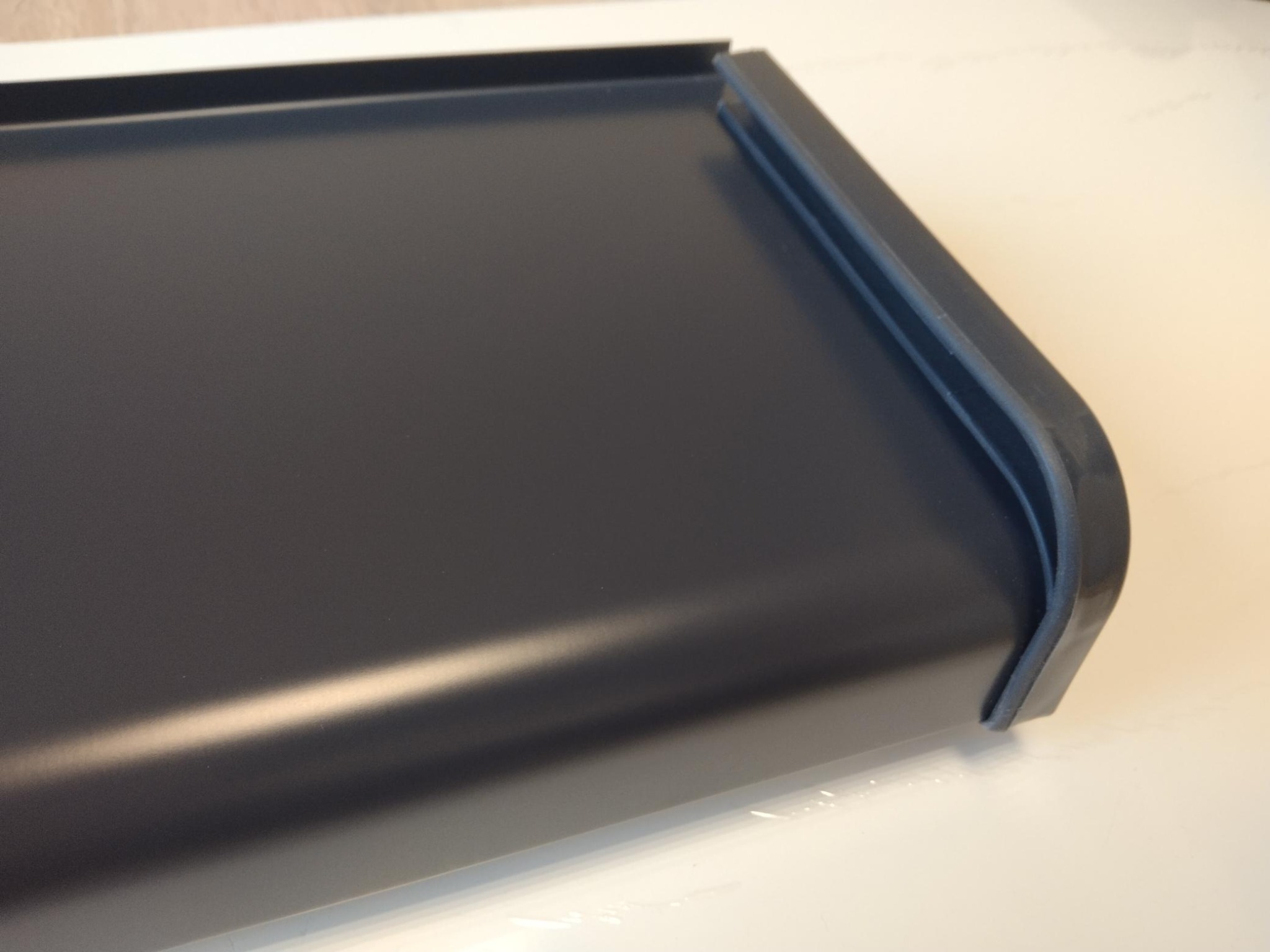 Fragment ciemnoszarego parapetu aluminiowego z charakterystycznym profilem krawędzi, leżącego na jasnej powierzchni.