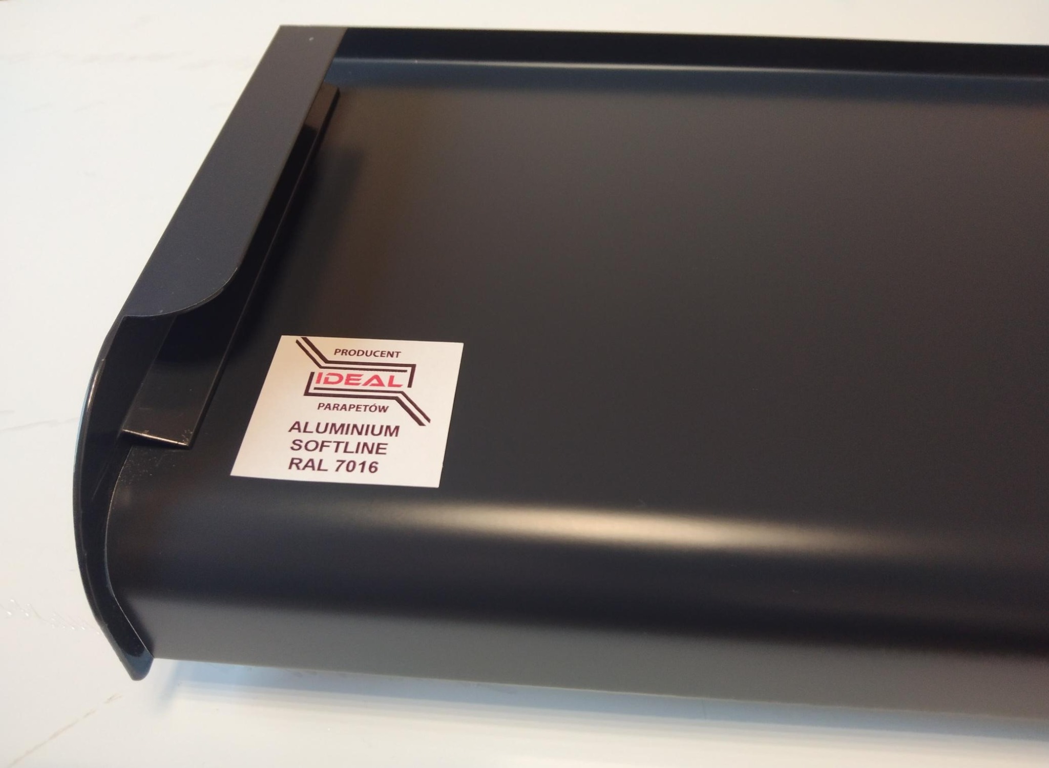 Szczegółowe ujęcie aluminiowego parapetu SOFTLINE RAL 7016 z naklejką producenta Ideal Parapetów.
