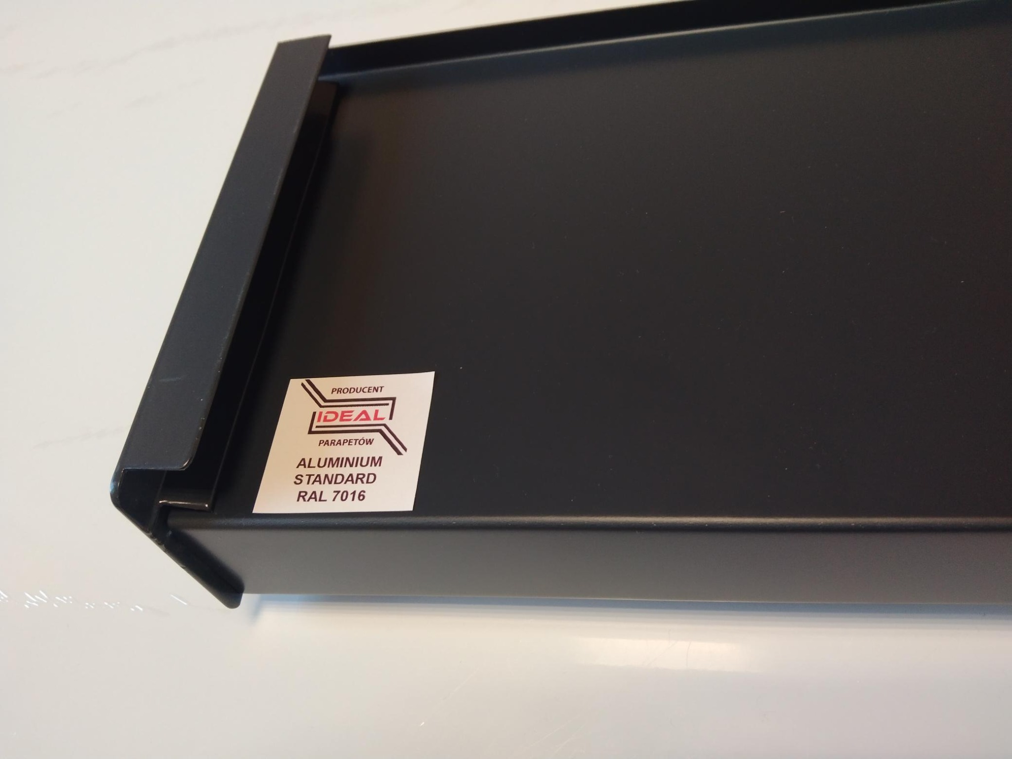 Ciemnoszary aluminiowy parapet z naklejoną etykietą producenta 'Ideal'
