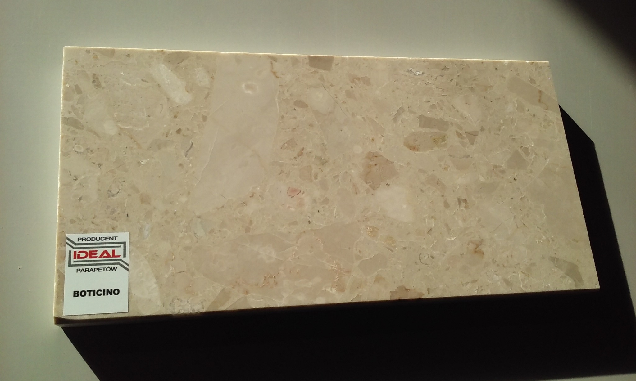 Próbka beżowego konglomeratu o nazwie Boticino, z widocznym logo producenta Ideal Parapetów.