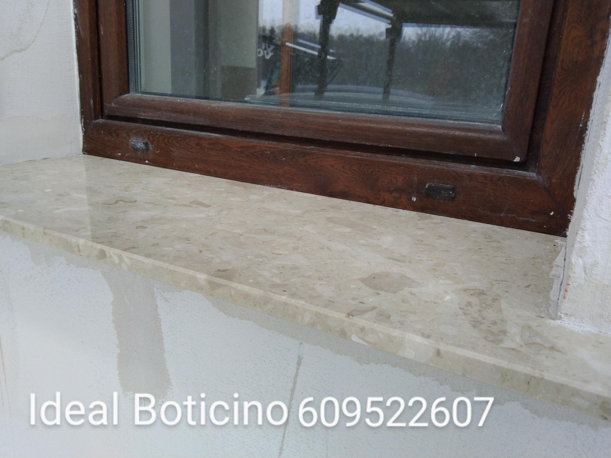 Beżowy parapet z konglomeratu imitującego marmur, zamontowany pod drewnianym oknem, widoczne ślady po montażu na ścianie.