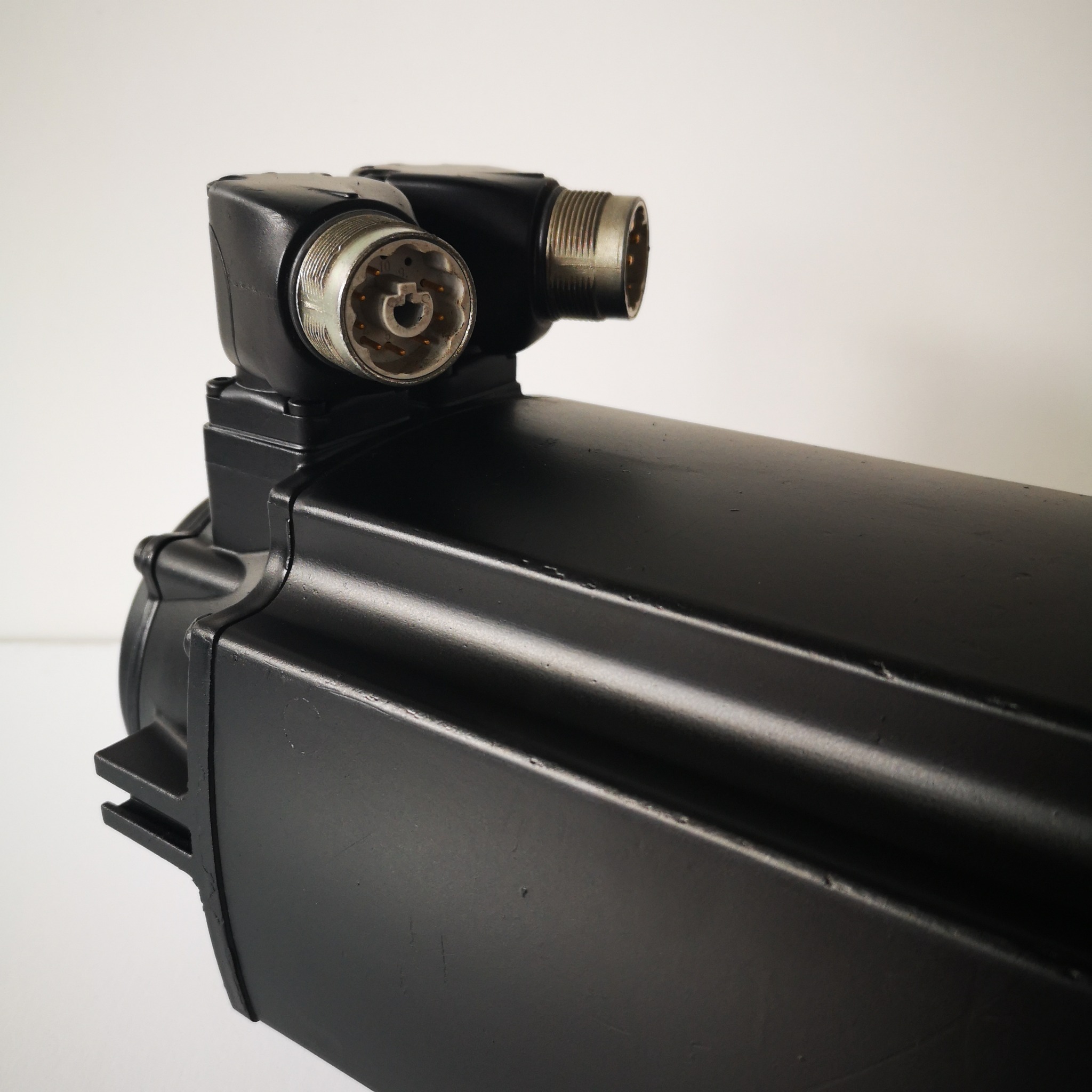 Czarny silnik elektryczny z dwoma złączami wtykowymi, widoczne piny wewnątrz złączy, na jednolitym, jasnym tle.