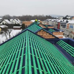 E&D Complex - Konstrukcja dachu z zielonymi łatami i czarną membraną, widok z góry na budowie w pochmurny dzień, w tle zabudowa jednorodzinna i las.