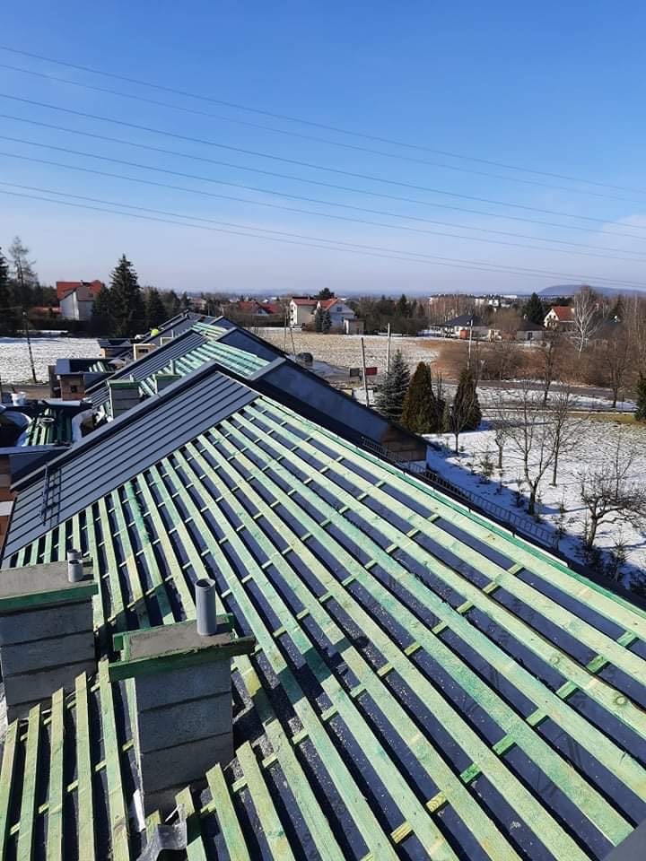 Konstrukcja dachu z łatami i kontrłatami przygotowana pod pokrycie, widok z góry na tle zimowego krajobrazu z zabudowaniami.