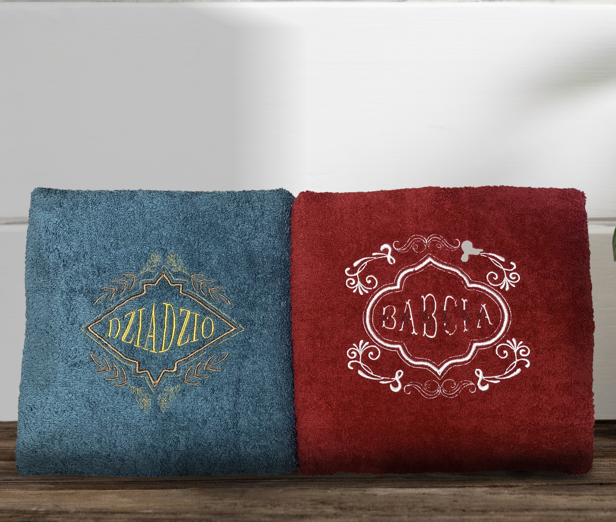 Dwa złożone ręczniki: turkusowy z haftowanym napisem 'Dziadziu' w złotej ramce i bordowy z haftowanym napisem 'Babcia' w białej, ozdobnej ramce.
