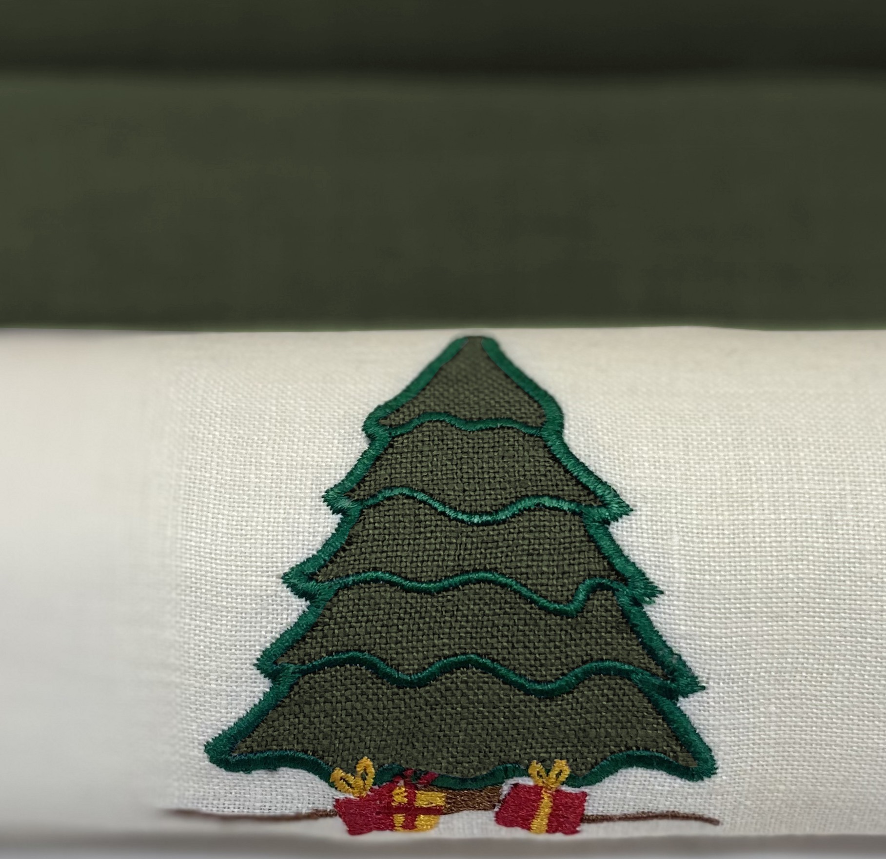 Aplikacja przedstawiająca haftowany motyw choinki z prezentami u podstawy, umieszczona na białym, tekstylnym podłożu.