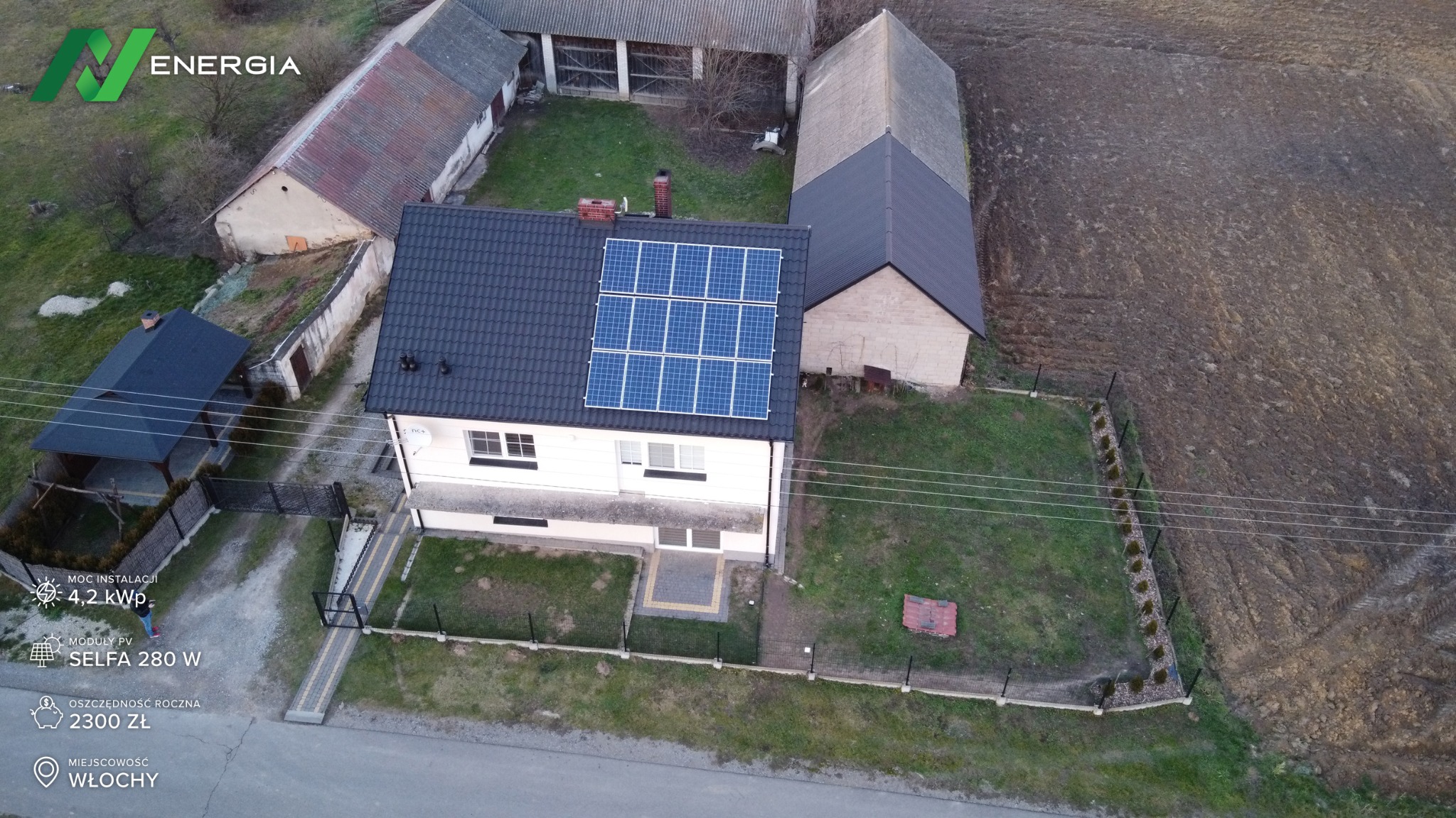 Widok z drona na dom jednorodzinny we Włochach z zamontowaną instalacją fotowoltaiczną na dachu, otoczony zabudowaniami gospodarczymi i polem.