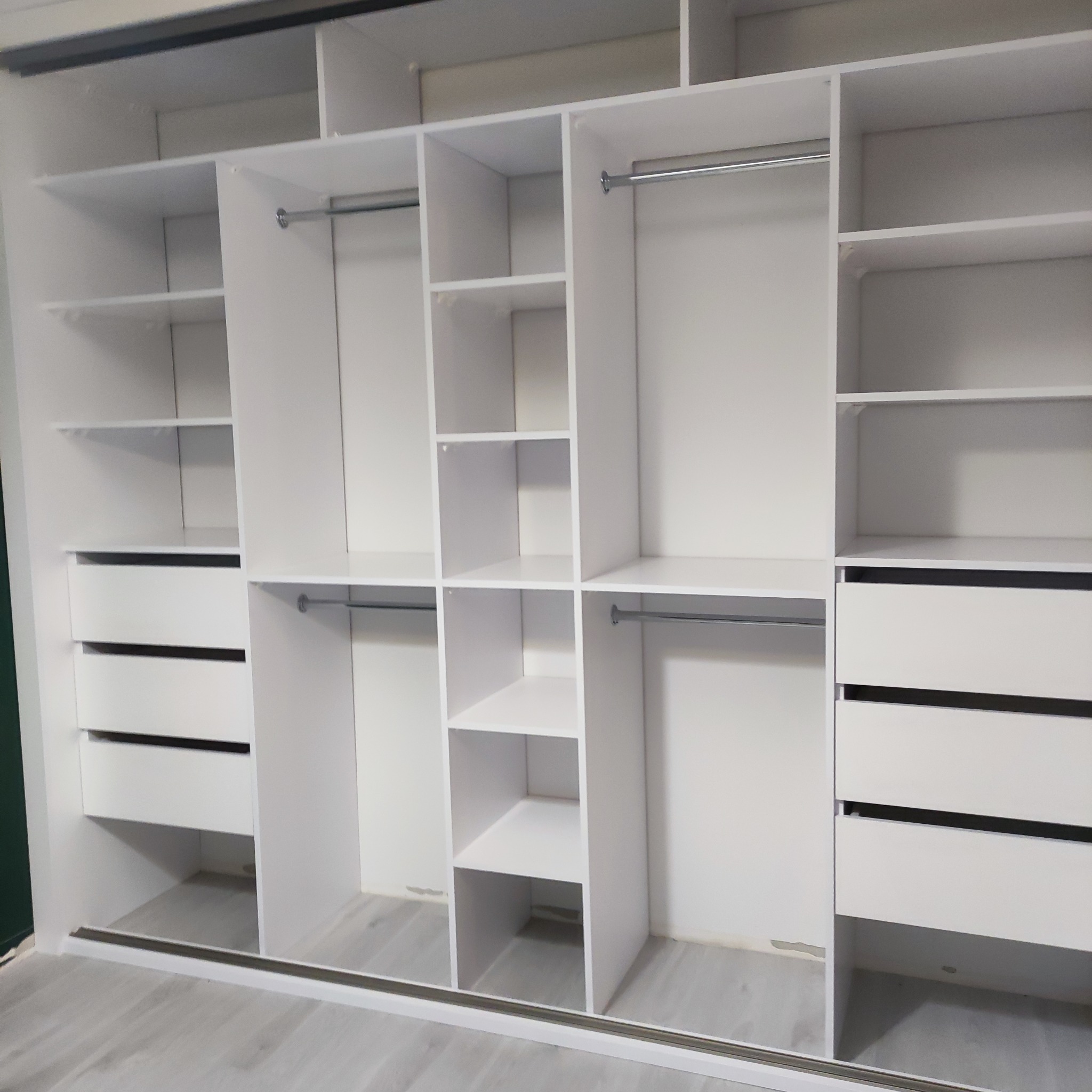 Wnętrze szafy przesuwnej z białymi półkami, drążkami na ubrania i szufladami, widok z bliska na system przechowywania.