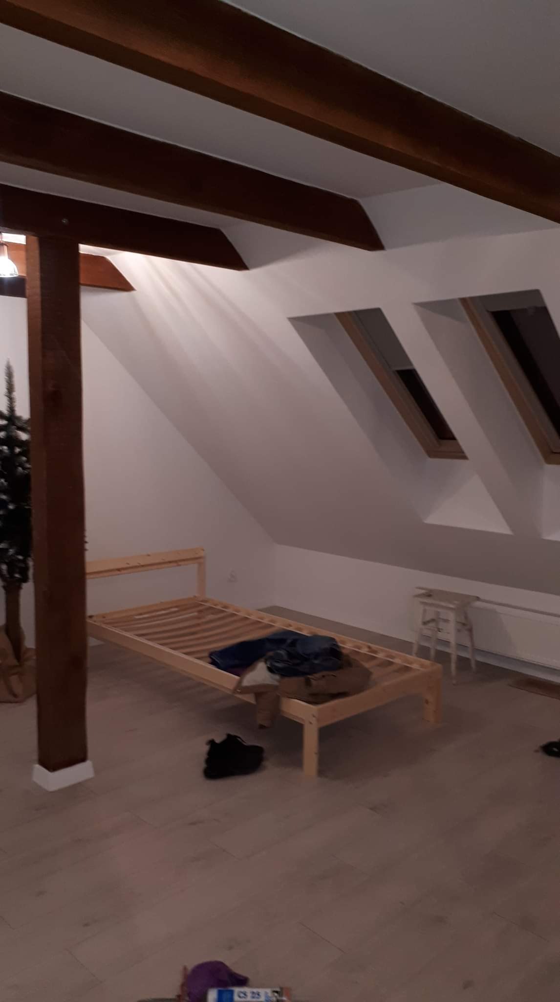 Poddasze w Gąskowie w trakcie prac: widoczne drewniane belki stropowe, stelaż łóżka, okna dachowe i przygotowane do położenia panele podłogowe.