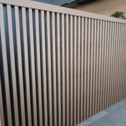 Panel ścienny z pionowych listew z jasnego drewna na czarnym tle, widok z boku, w tle roślina doniczkowa.