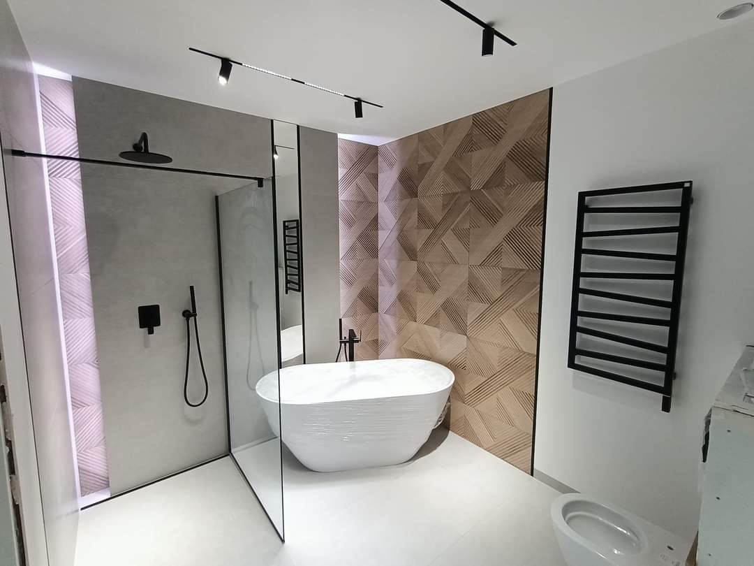 Nowoczesna łazienka z kabiną prysznicową typu walk-in, wolnostojącą wanną owiniętą folią ochronną, grzejnikiem drabinkowym w kolorze czarnym i dekoracyjną ścianą z drewnopodobnych paneli 3D.