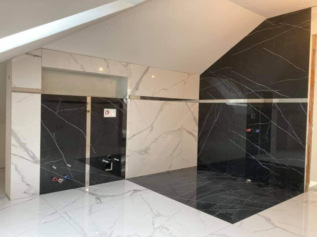 Nowoczesna łazienka w trakcie wykańczania z czarno-białymi płytkami imitującymi marmur na ścianach i podłodze, widoczne instalacje wodne i fragment sufitu ze światłem.