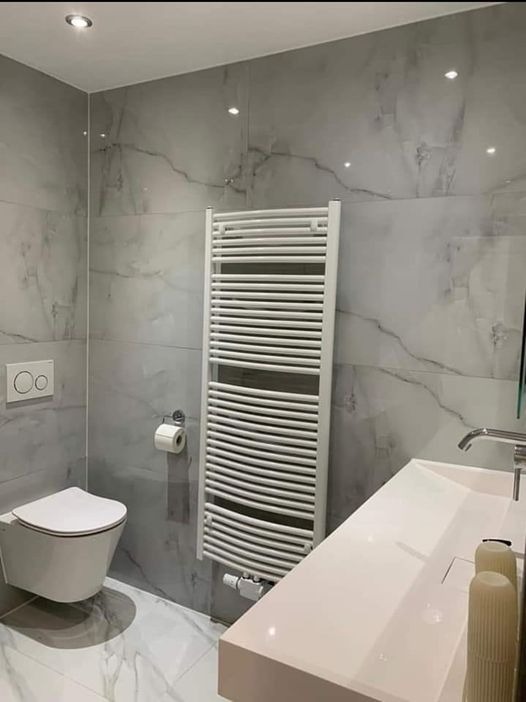 Nowoczesna łazienka z marmurowymi płytkami, podwieszaną toaletą z podwójnym przyciskiem spłukiwania, grzejnikiem drabinkowym i umywalką nablatową.