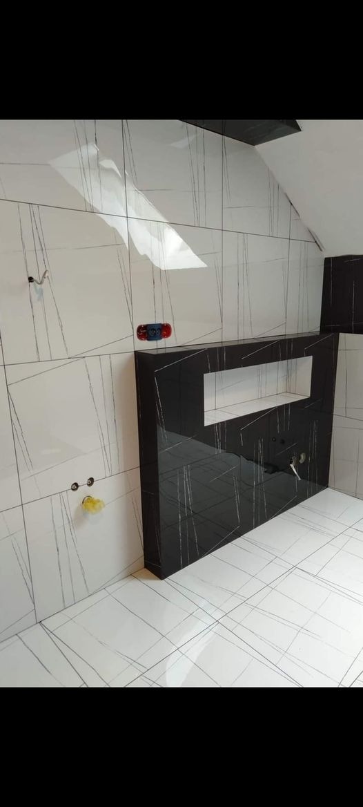 Nowoczesna łazienka z białymi płytkami imitującymi marmur z szarymi żyłami oraz czarnym blatem umywalkowym z wnęką, widoczne przyłącza wodne.