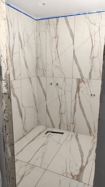 Płytki imitujące marmur w kabinie prysznicowej w trakcie montażu, widoczne otwory na armaturę i niedokończone wykończenie ściany.