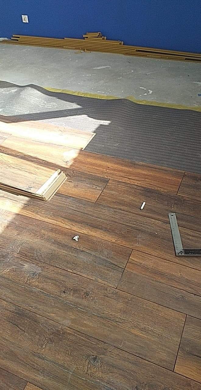 Fragment podłogi z paneli imitujących drewno w trakcie montażu, widoczna podkładka, przycięte panele oraz kątownik.