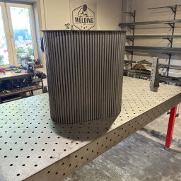 WELDING Łukasz Kułak - Metalowa konstrukcja z rurek na perforowanym stole spawalniczym w warsztacie, widoczne narzędzia i logo firmy spawalniczej w tle.