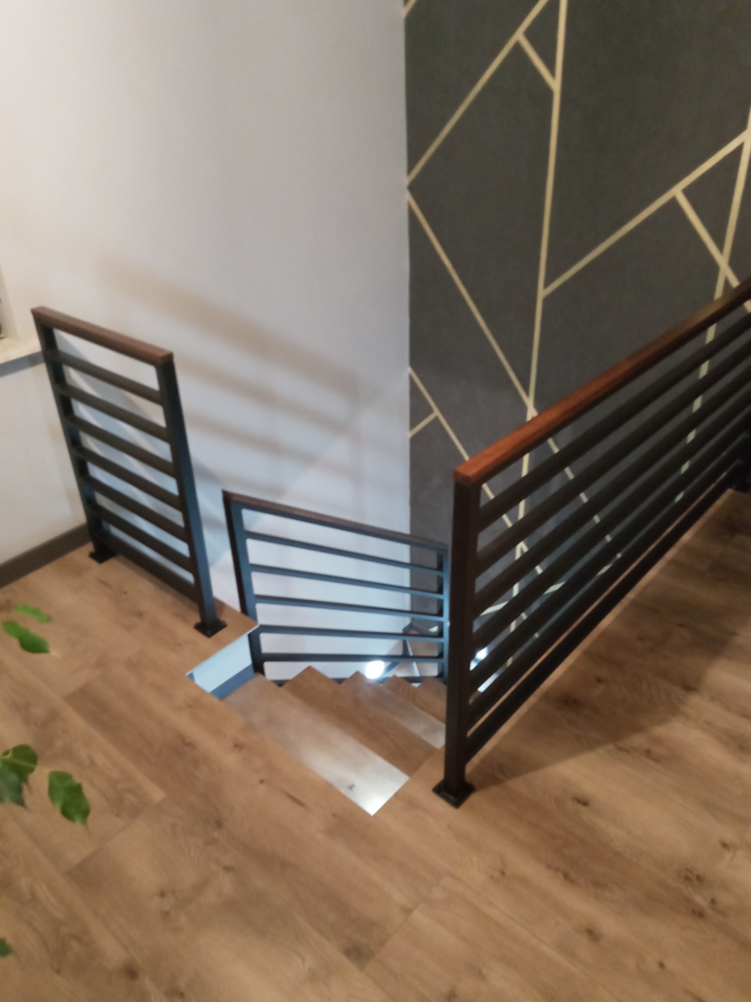 Nowoczesne schody z metalowymi balustradami z drewnianym wykończeniem w domu w Radomsku, widok z góry na drewniane stopnie i podłogę.