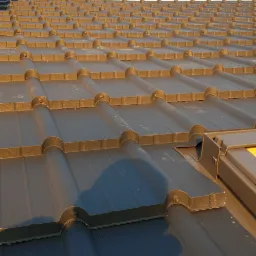 Nowy, grafitowy dach z blachodachówki modułowej, widok z dołu, z widocznym elementem okna dachowego, w tle błękitne niebo.