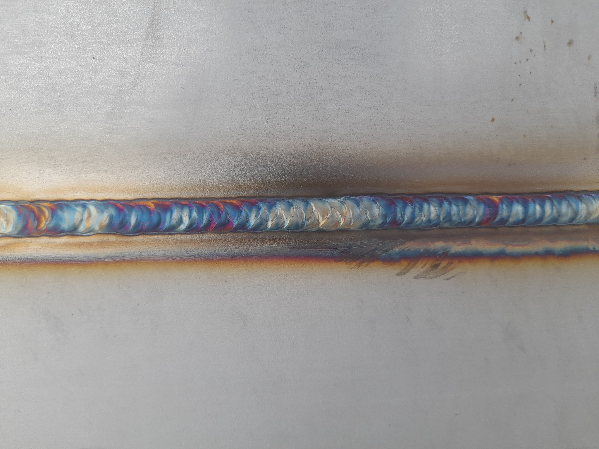 Świeżo wykonany spaw na metalowej powierzchni, widoczne tęczowe przebarwienia termiczne.