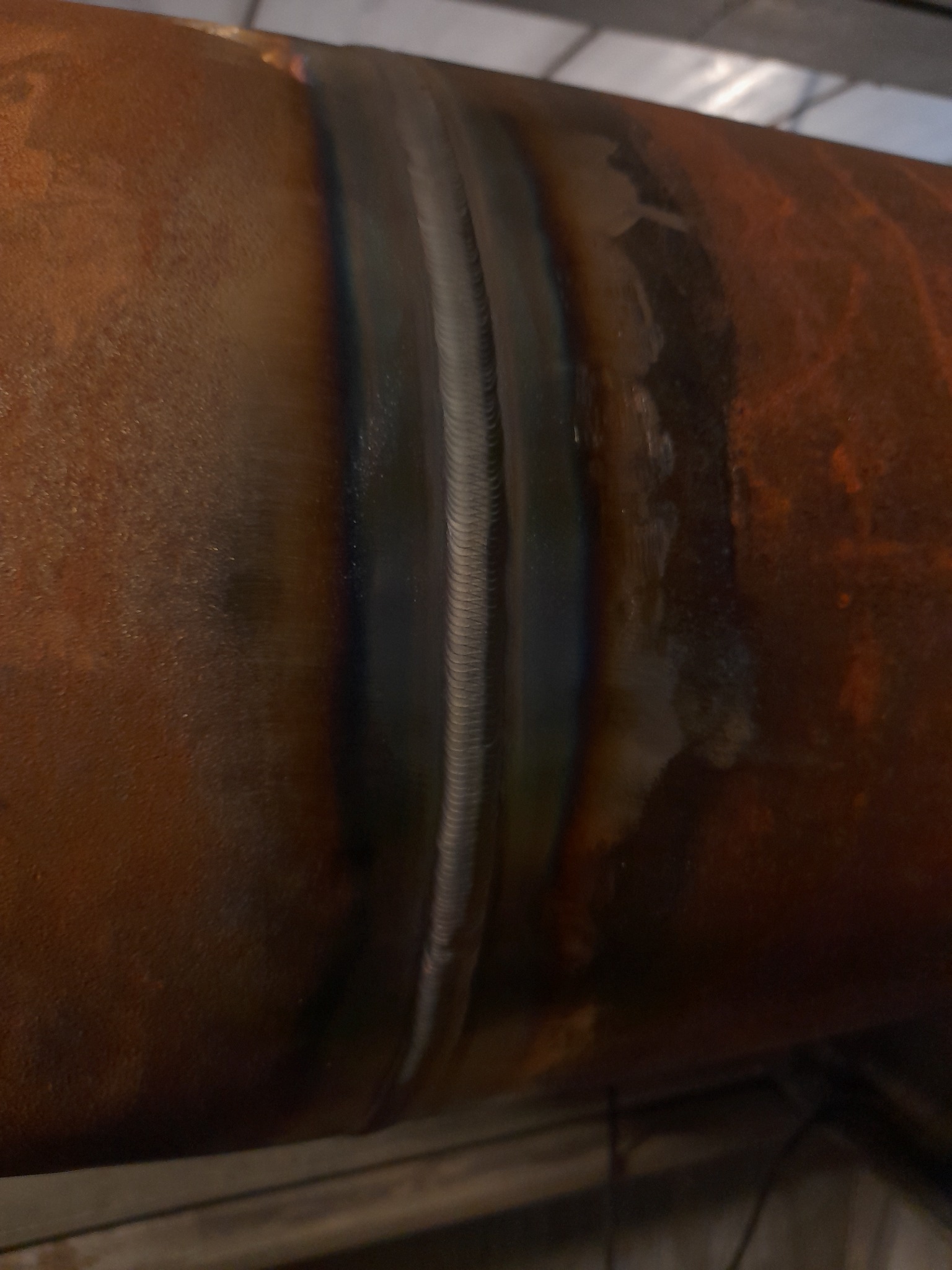 Spoina na rdzewiejącej rurze, widoczne ślady obróbki termicznej i zmiany kolorów metalu.