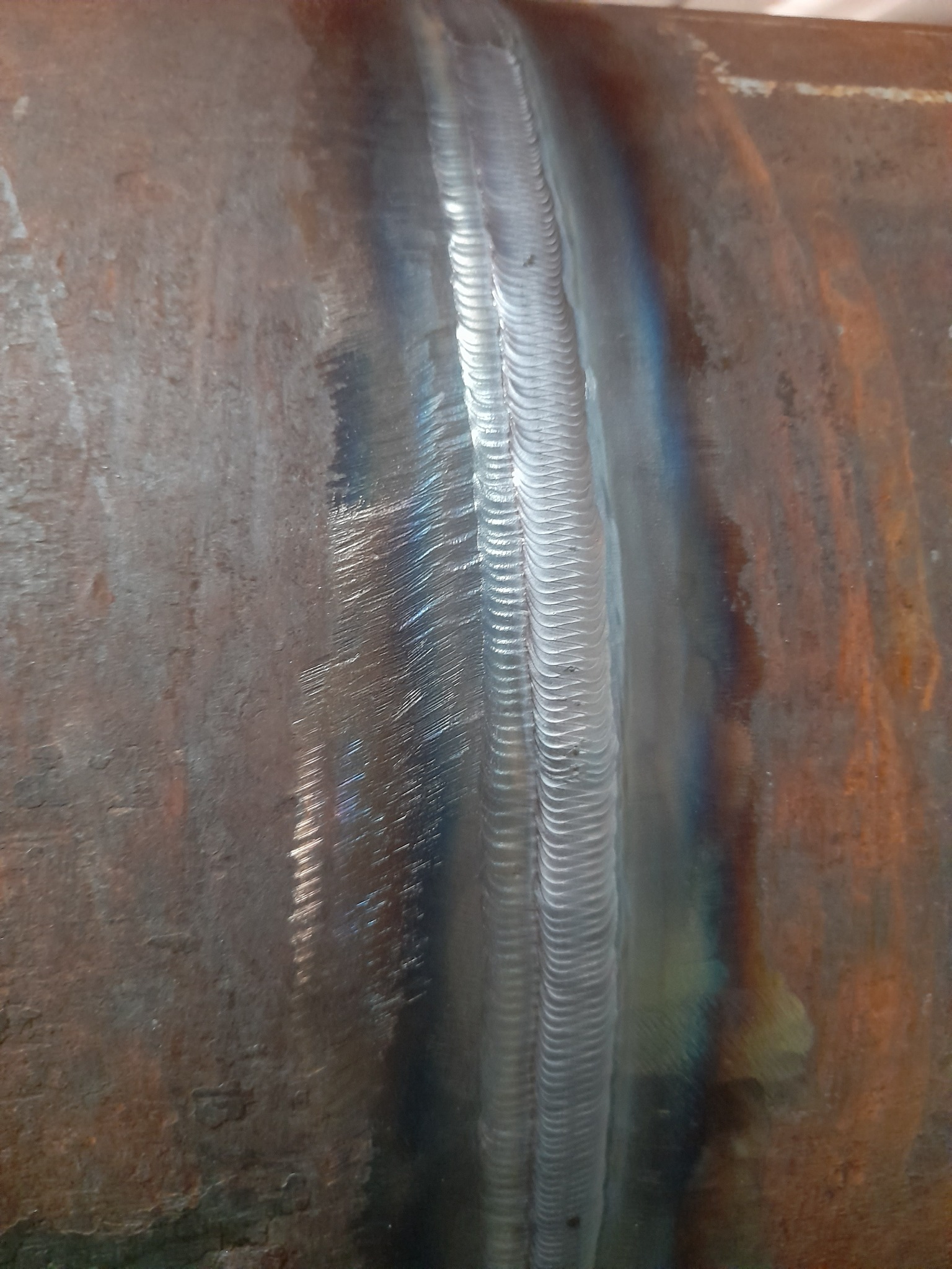 Spoina na rdzewiejącej rurze, widoczna struktura spawu z charakterystycznymi śladami po elektrodzie.