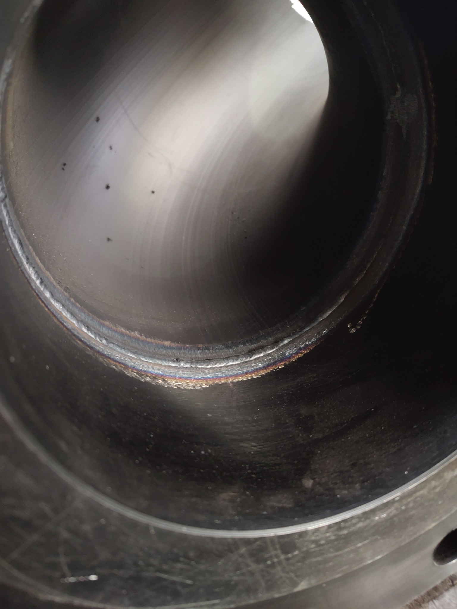 Wnętrze metalowej rury z widocznym, świeżo wykonanym spoinem obwodowym, ukazującym tęczowe zabarwienie w miejscu łączenia.