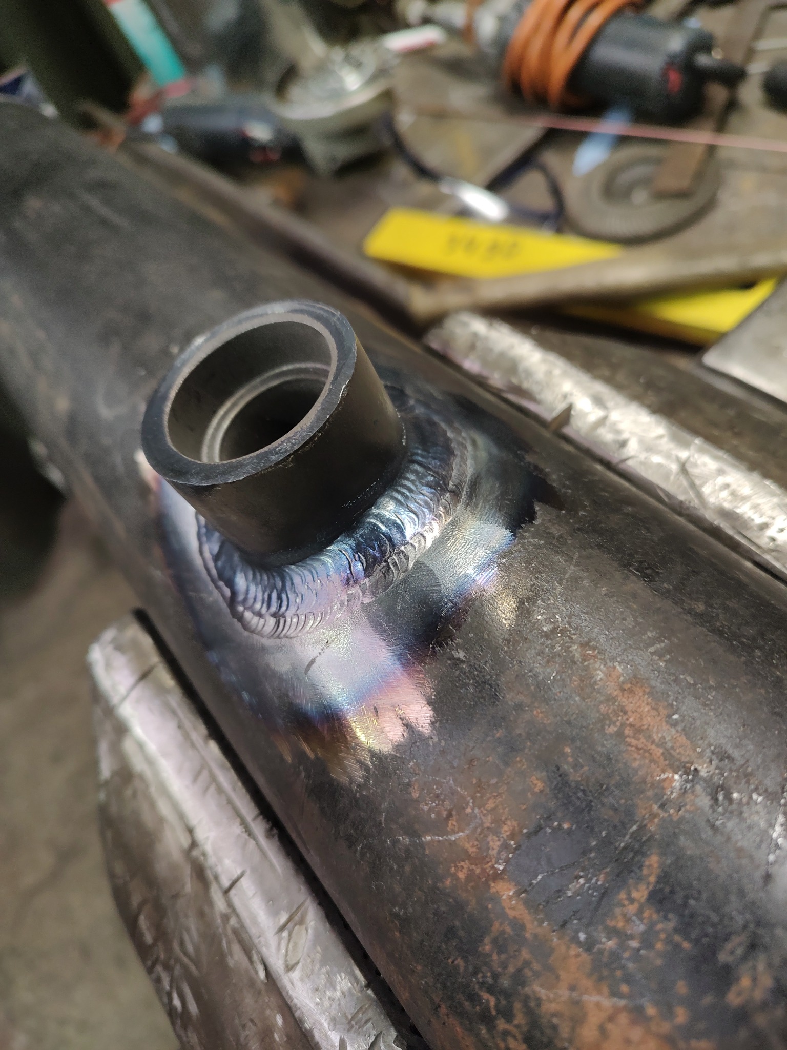 Spoina na rurze z zamontowanym króćcem, widoczne ślady ciepła i przebarwienia, warsztatowe tło.