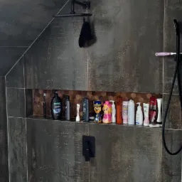 Ciemna, grafitowa kabina prysznicowa z półką wnękową, na której stoją kosmetyki i figurki z bajki Psi Patrol, czarna deszczownica i bateria prysznicowa.