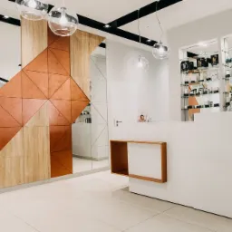 Nowoczesne wnętrze recepcji z geometryczną ścianą z luster i paneli drewnianych w odcieniach brązu, biała lada recepcyjna z drewnianymi akcentami, szklane półki z kosmetykami i bukiet róż w tle...