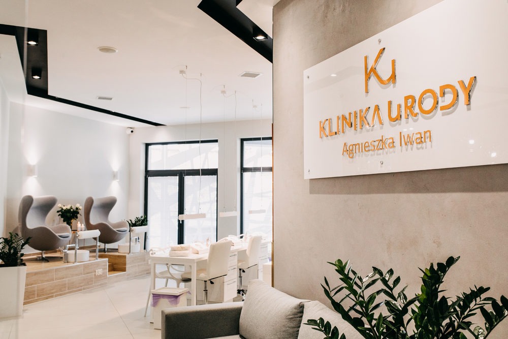 Jasne wnętrze gabinetu z recepcją, stanowiskami do manicure i pedicure oraz fotelami relaksacyjnymi, widoczna tabliczka z nazwą 'Klinika Urody Agnieszka Iwan'.