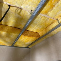 RN-BUD SERHII ZOSYK - Poddasze ocieplone wełną mineralną, widoczne metalowe profile konstrukcyjne. Kabel elektryczny w peszlu w rogu. Ocieplenie w kolorze żółtym, świeżo położone.